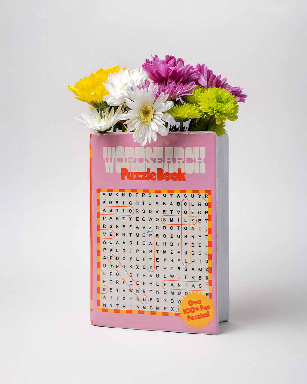 side view of pink word search puzzle book shaped ceramic vase with flowers inside