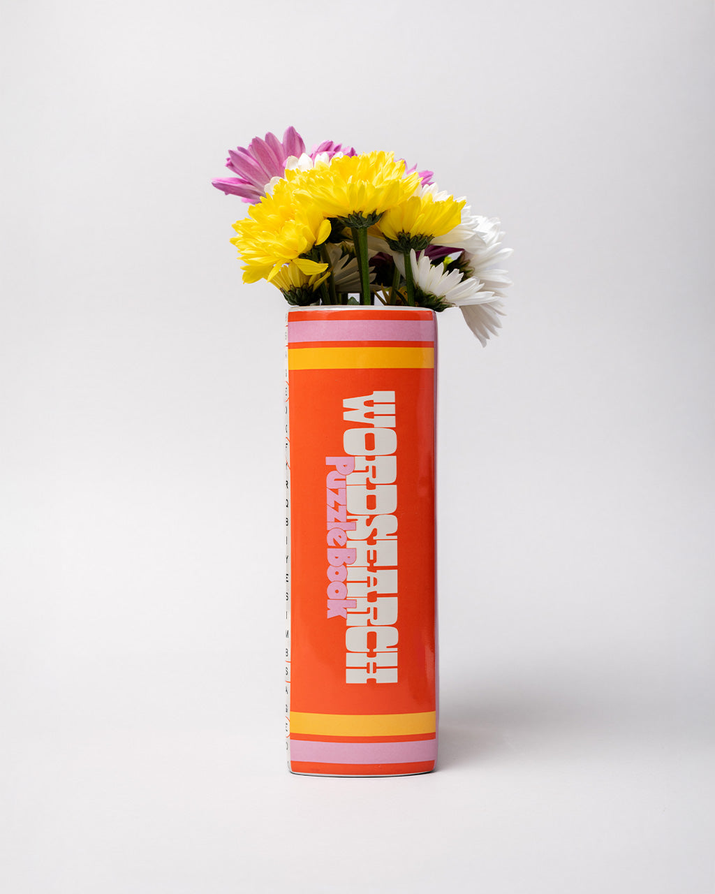 spine of pink word search puzzle book shaped ceramic vase with flowers inside