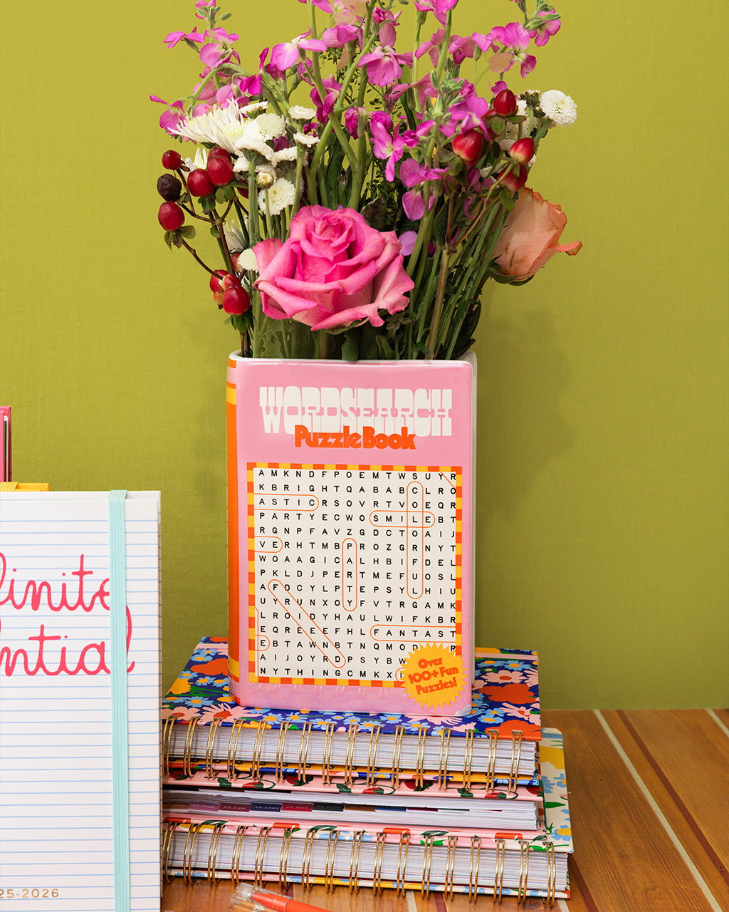 pink word search puzzle book shaped ceramic vase on a stack of ban.do planners