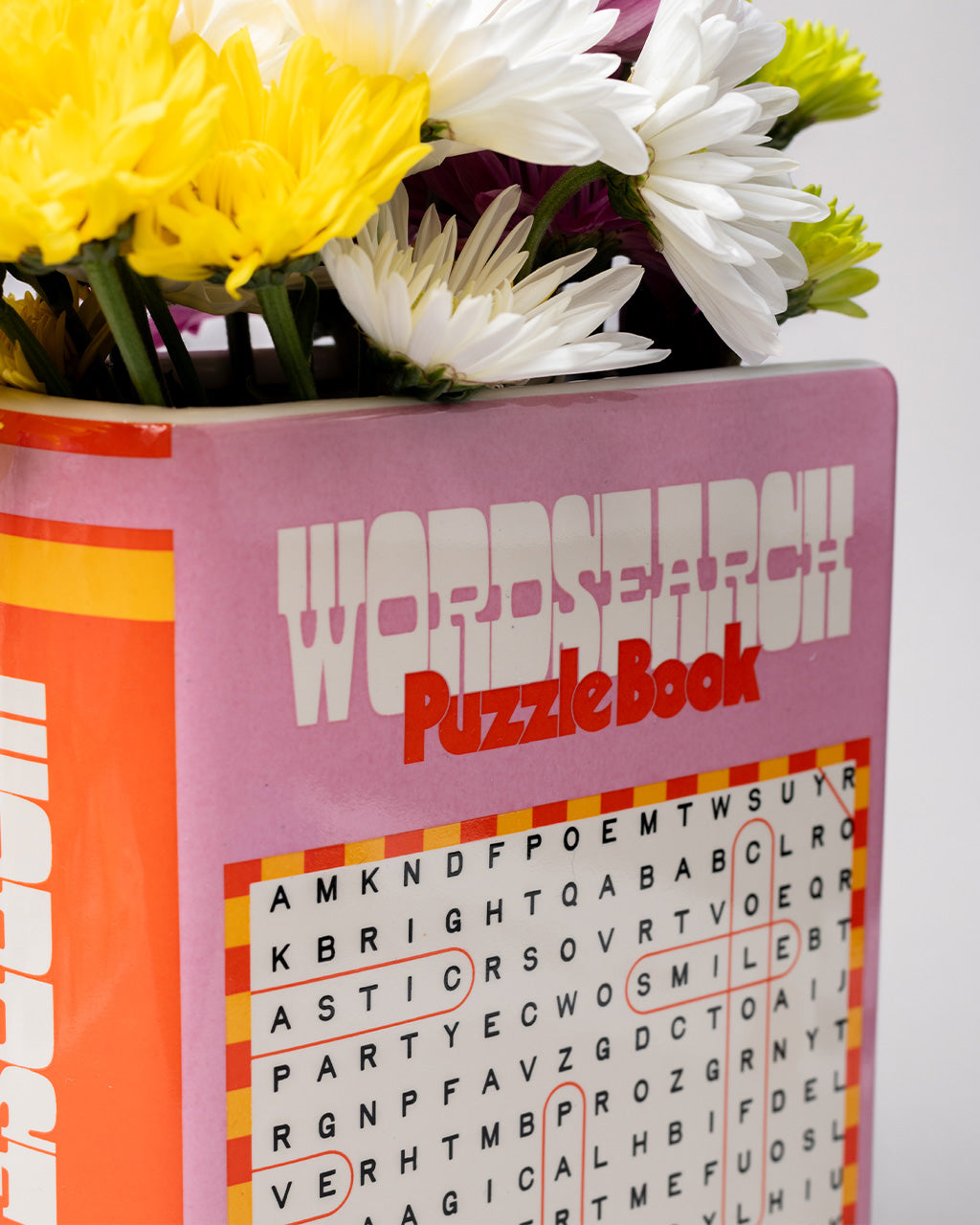 up close of pink word search puzzle book shaped ceramic vase with flowers inside