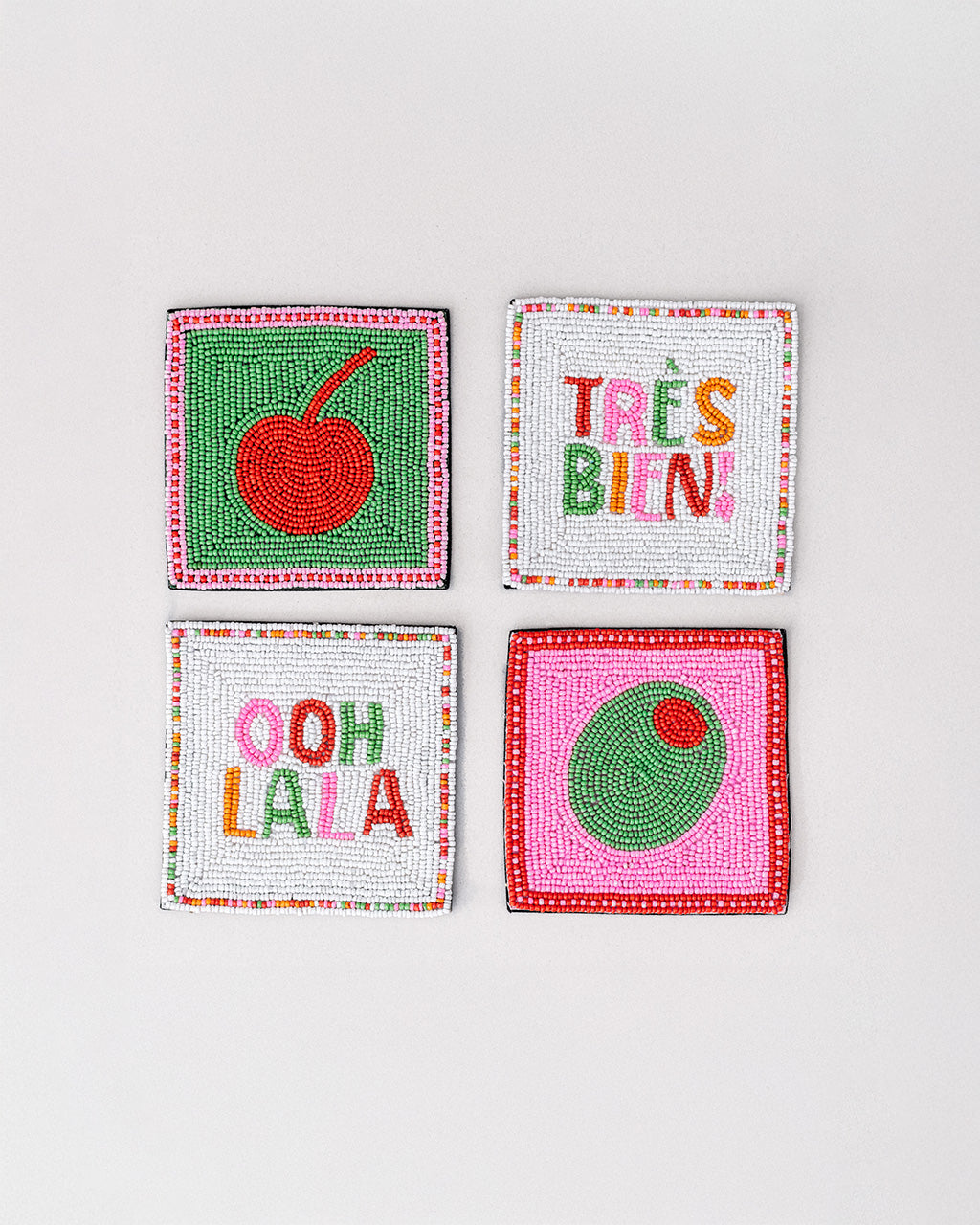 set of 4 beaded coasters: green beaded with cherry print, white with colorful beaded 'tres bien!', white with colorful beaded 'ooh lala', and pink with beaded olive.