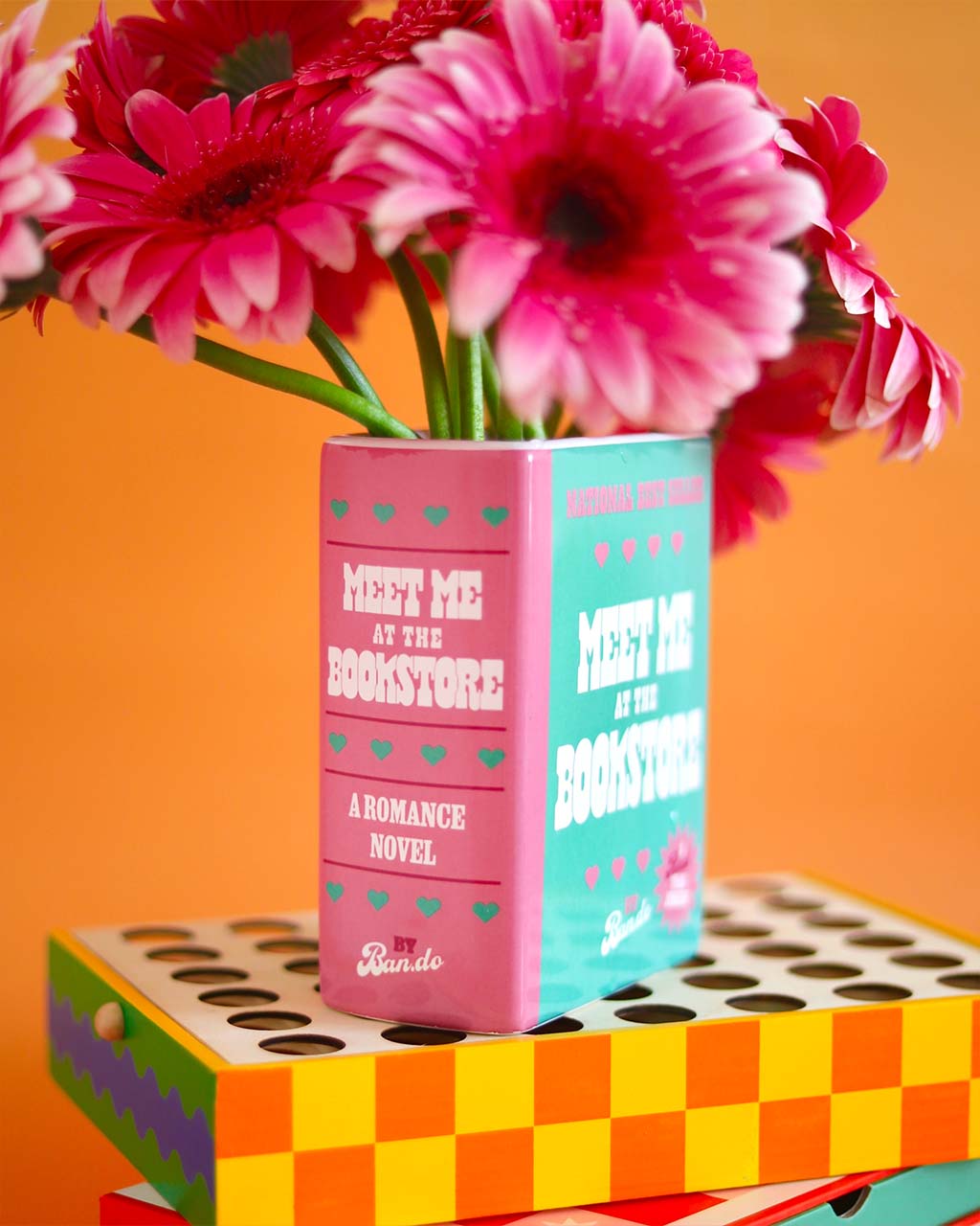 side view of green and pink book ceramic vase: meet me at the bookstore by ban.do with pink flowers inside