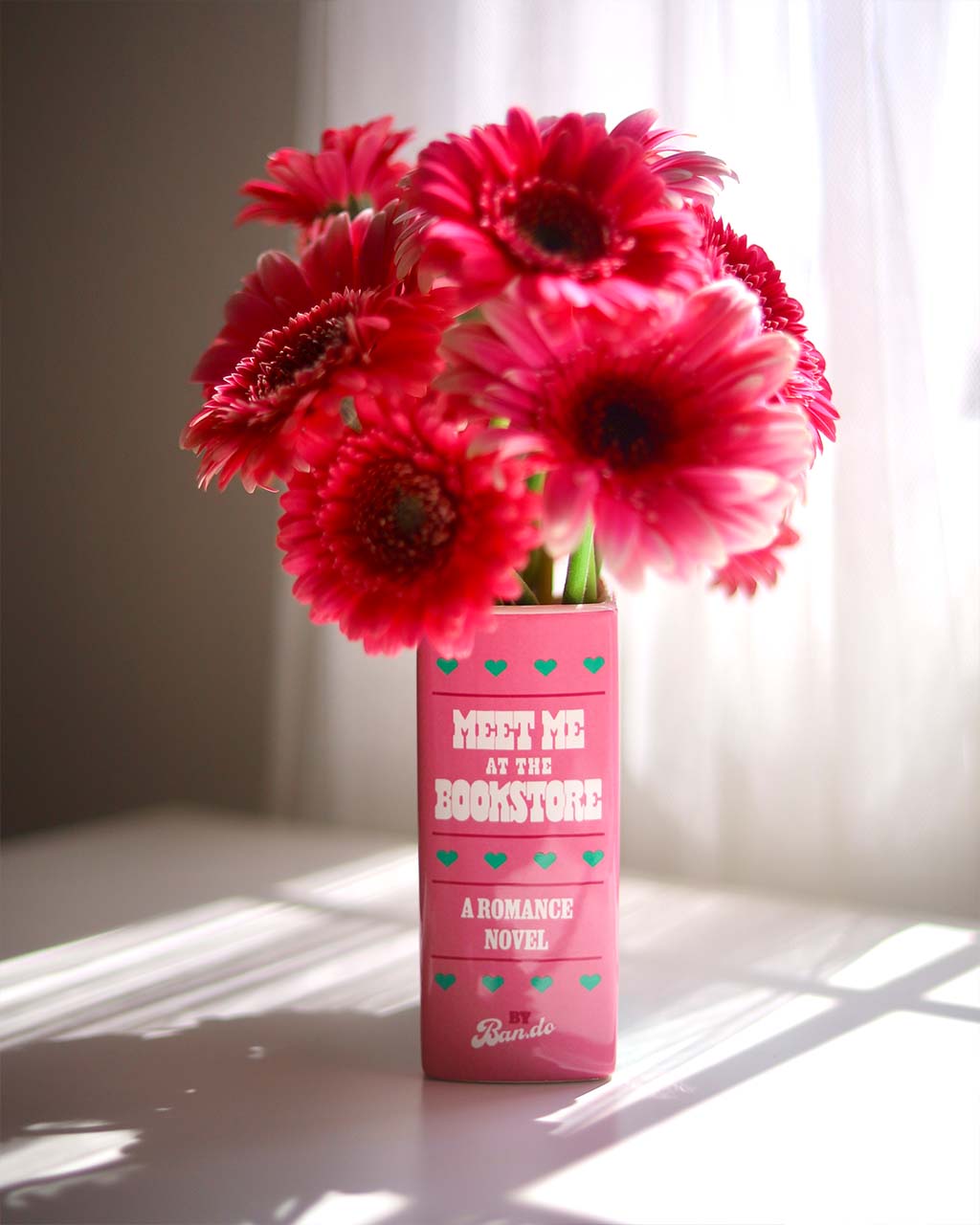 side view of green and pink book ceramic vase: meet me at the bookstore by ban.do with pink flowers inside