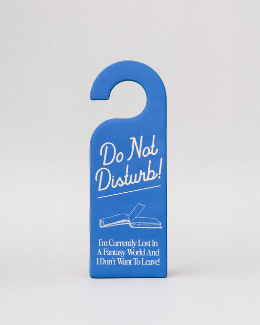 blue bookmark in the shape of a door hanger with white 'do not disturb!i'm currently lost in a fantasy world and i don't want to leave!' across the front