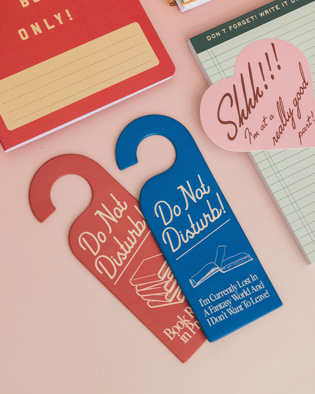 blue bookmark in the shape of a door hanger with white 'do not disturb!i'm currently lost in a fantasy world and i don't want to leave!' across the front on a pink ground