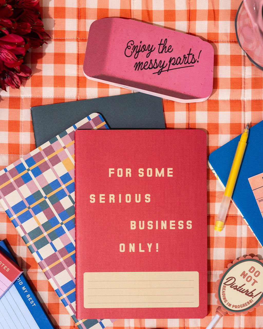 realistic eraser notepad with 'enjoy the messy parts' across the front on a gingham background